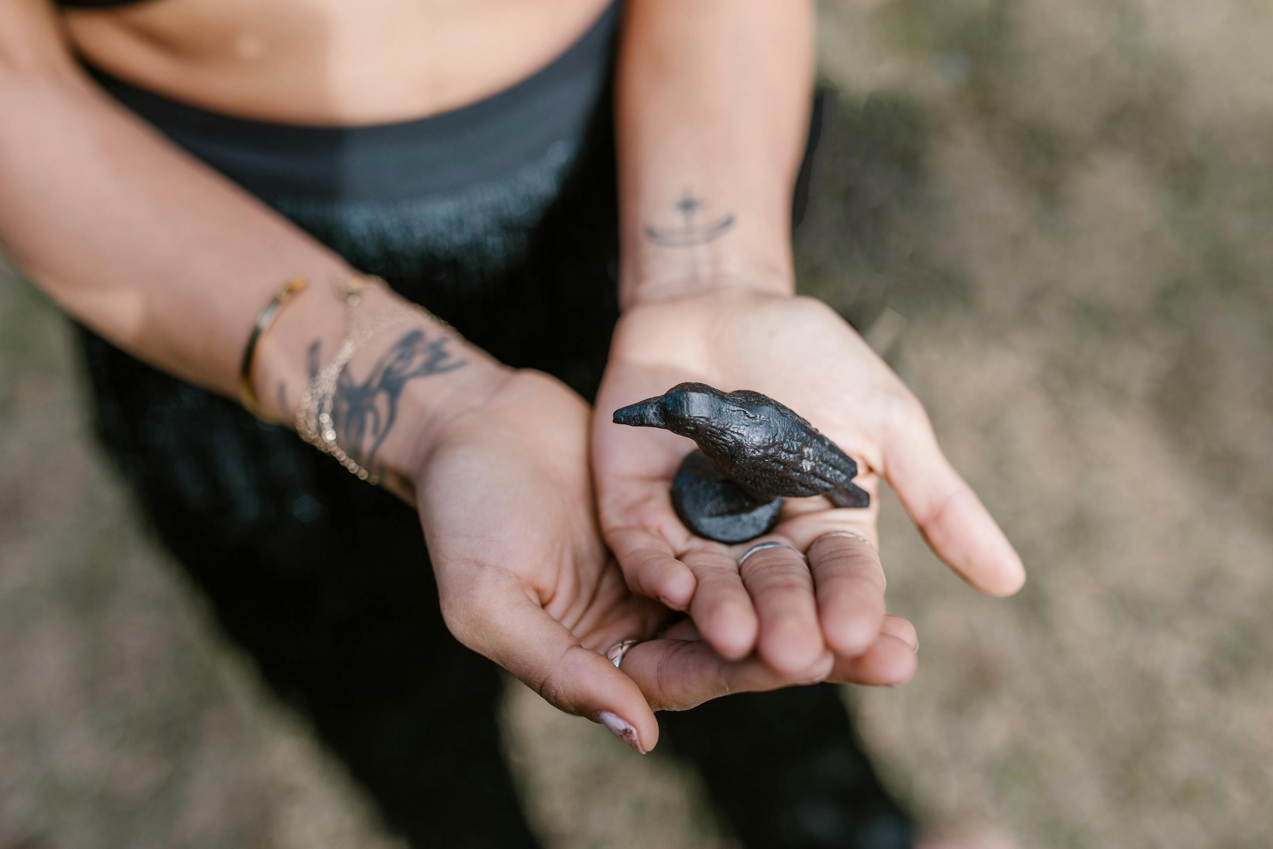 Close-up of hands holding a raven statue, symbolizing magic and spirituality outdoors.